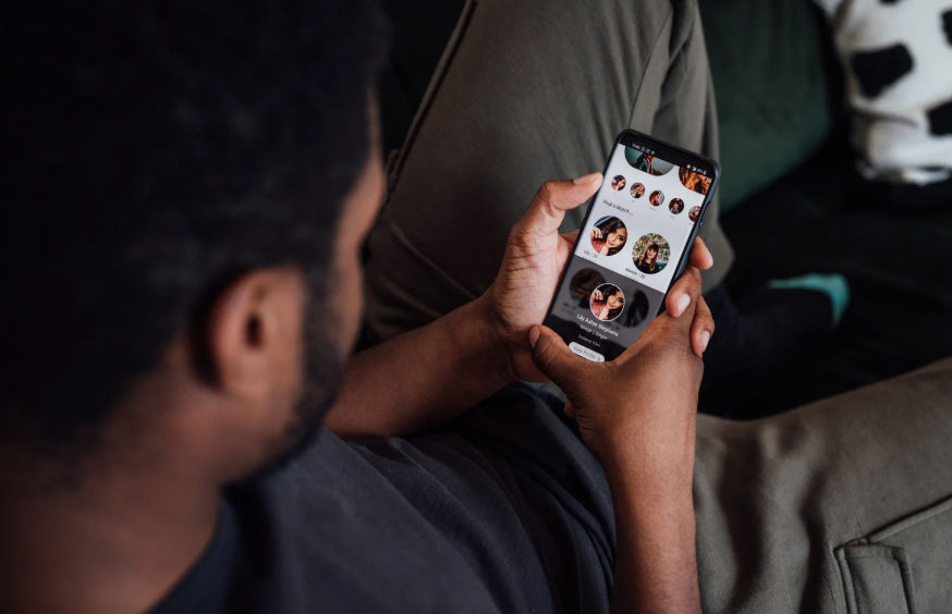 Image of a guy with dark hair, a beard, and browsing a dating site on his phone